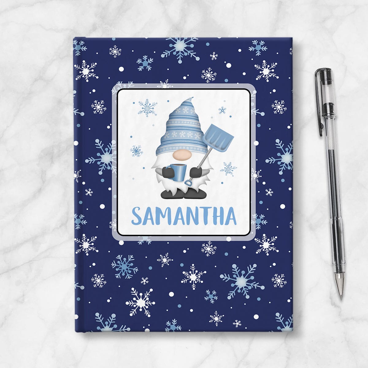 Personalized Blue Winter Gnome Journal at Artistically Invited. A custom book designed with an adorable gnome holding a hot beverage and a snow shovel with light blue snowflakes floating around him in a white rectangular design on the front of the book, with your name personalized in blue in a cute all capital letters font below the gnome. The background design that wraps around the cover of the book features a beautiful pattern whimsical snowflakes in white and blue over a navy blue background color.