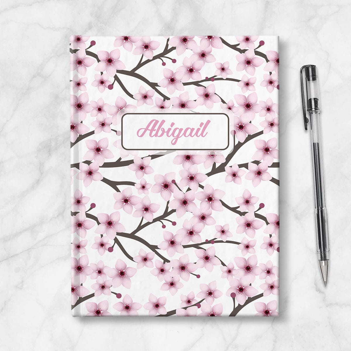 Personalized Cherry Blossom Journal at Artistically Invited. Image shows the book on a countertop with a pen next to it. 