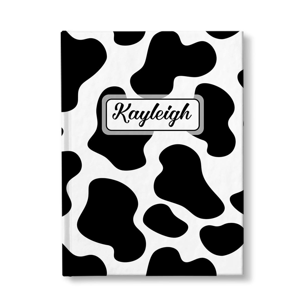 Personalized Cow Print Journal at Artistically Invited. A custom book illustrated with a bold and sleek black and white cow print pattern that wraps around the cover of the journal. Your personalized name is custom printed in a cute script font in black within a white rectangular design on the front of the book over the cow print background.