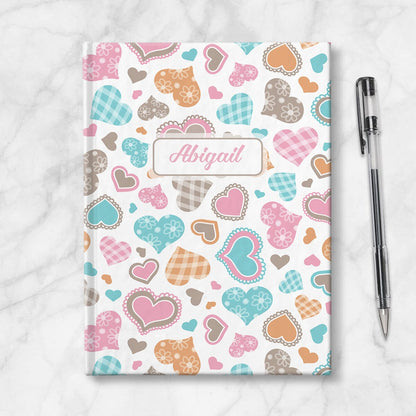 Personalized Cutesy Hearts Pattern Journal at Artistically Invited. Image shows book on countertop with a pen next to it.
