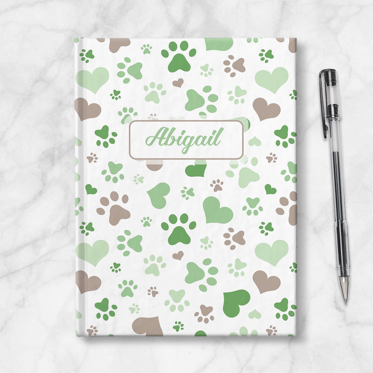 Personalized Green Hearts and Paw Prints Journal at Artistically Invited. Image shows the book on a countertop next to a pen.