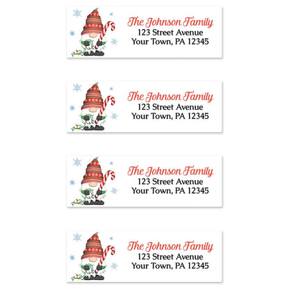 Holiday Candy Cane Gnome Address Labels at Artistically Invited. Sheet of 4 labels. These address labels are designed with an illustration of a cute gnome wearing a festive red hat while holding a large candy cane and a string of Christmas lights with snowflakes around him. Your personalized return address is custom printed in red and black over white to the right of the holiday-themed gnome.