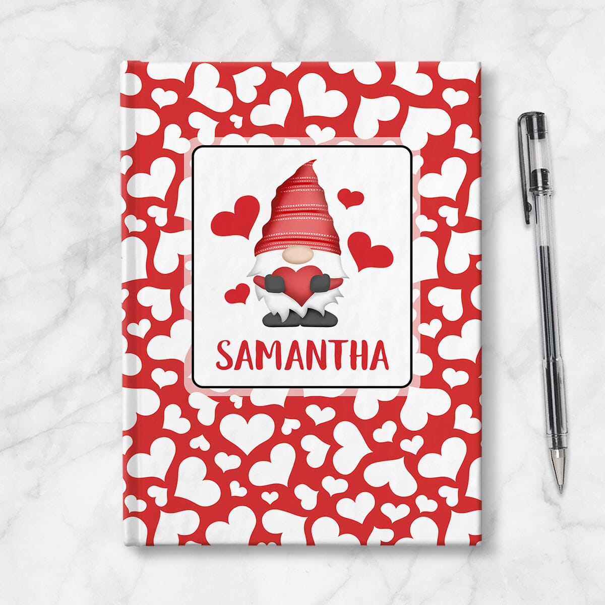 Personalized Red Hearts Gnome Journal at Artistically Invited. A custom book designed with an adorable gnome holding a red heart with 4 hearts floating around him in a white rectangular design on the front of the book, with your name personalized in red below the gnome. The background design that wraps around the cover of the book features a red background color filled with cute multi-directional white hearts of different sizes. Image shows the book next to a pen.