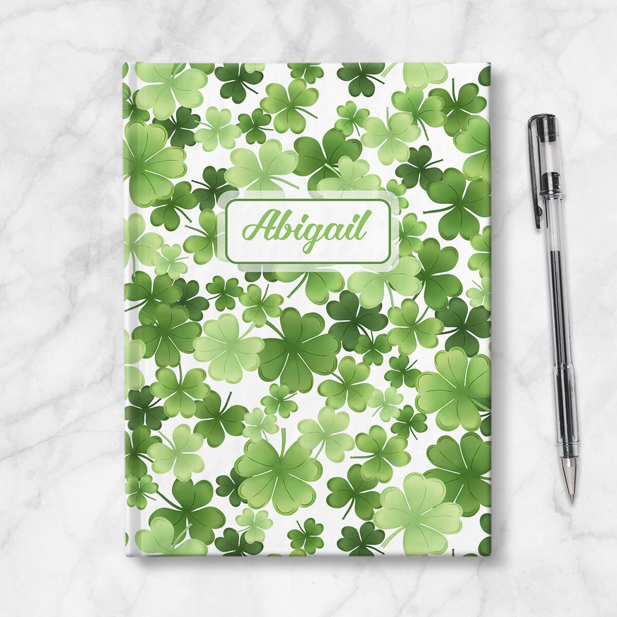 Personalized Shamrocks and 4-Leaf Clovers Journal at Artistically Invited. Image shows book on table with a pen next to it.