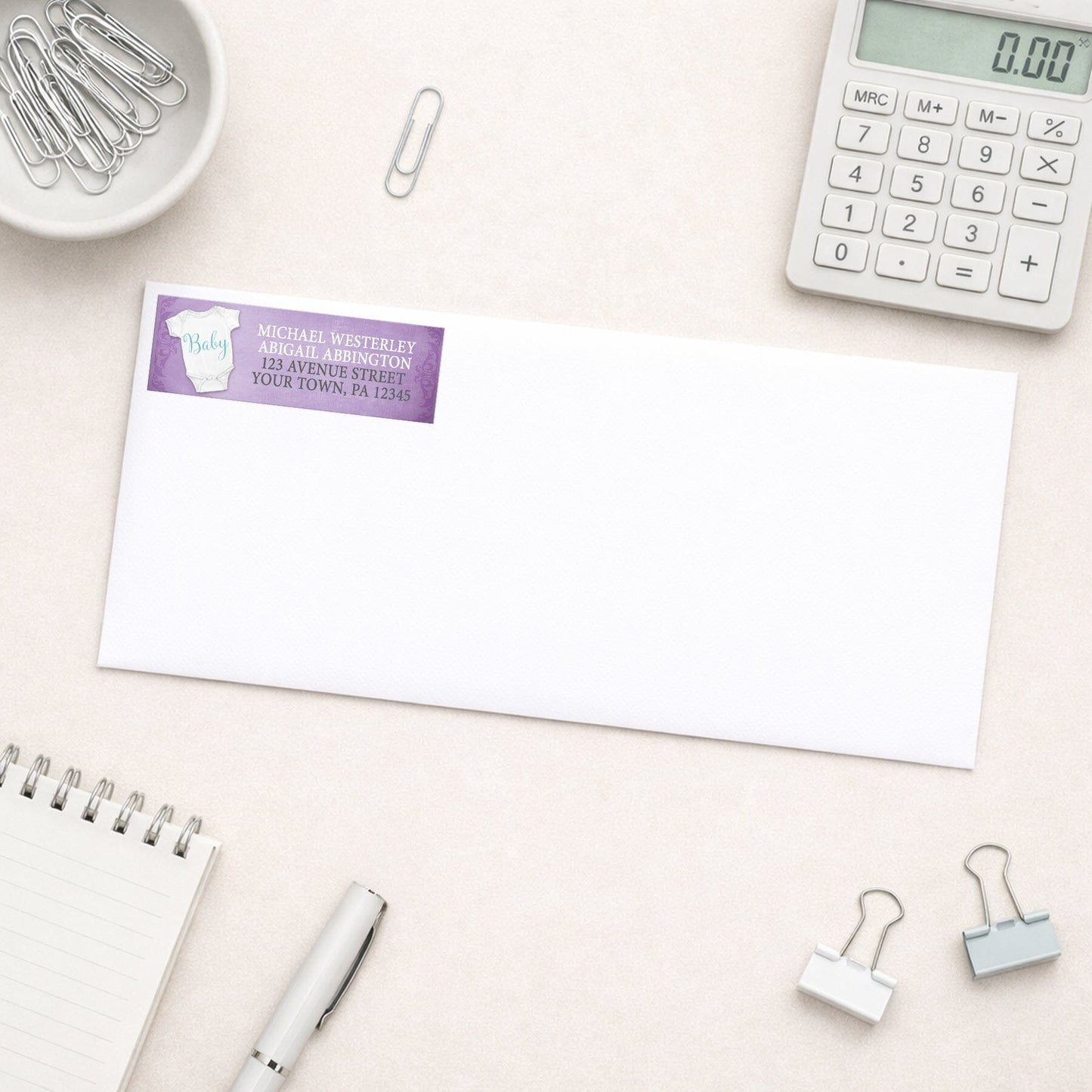 Baby Bodysuit on Purple Address Label shown on a white envelope with office supplies