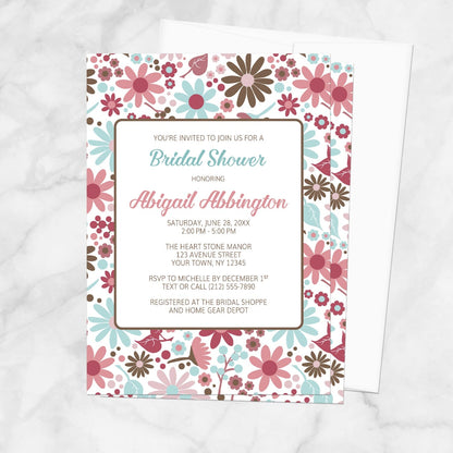 Bridal shower invitation with a pink, blue, and brown flowers design, shown on a marble surface