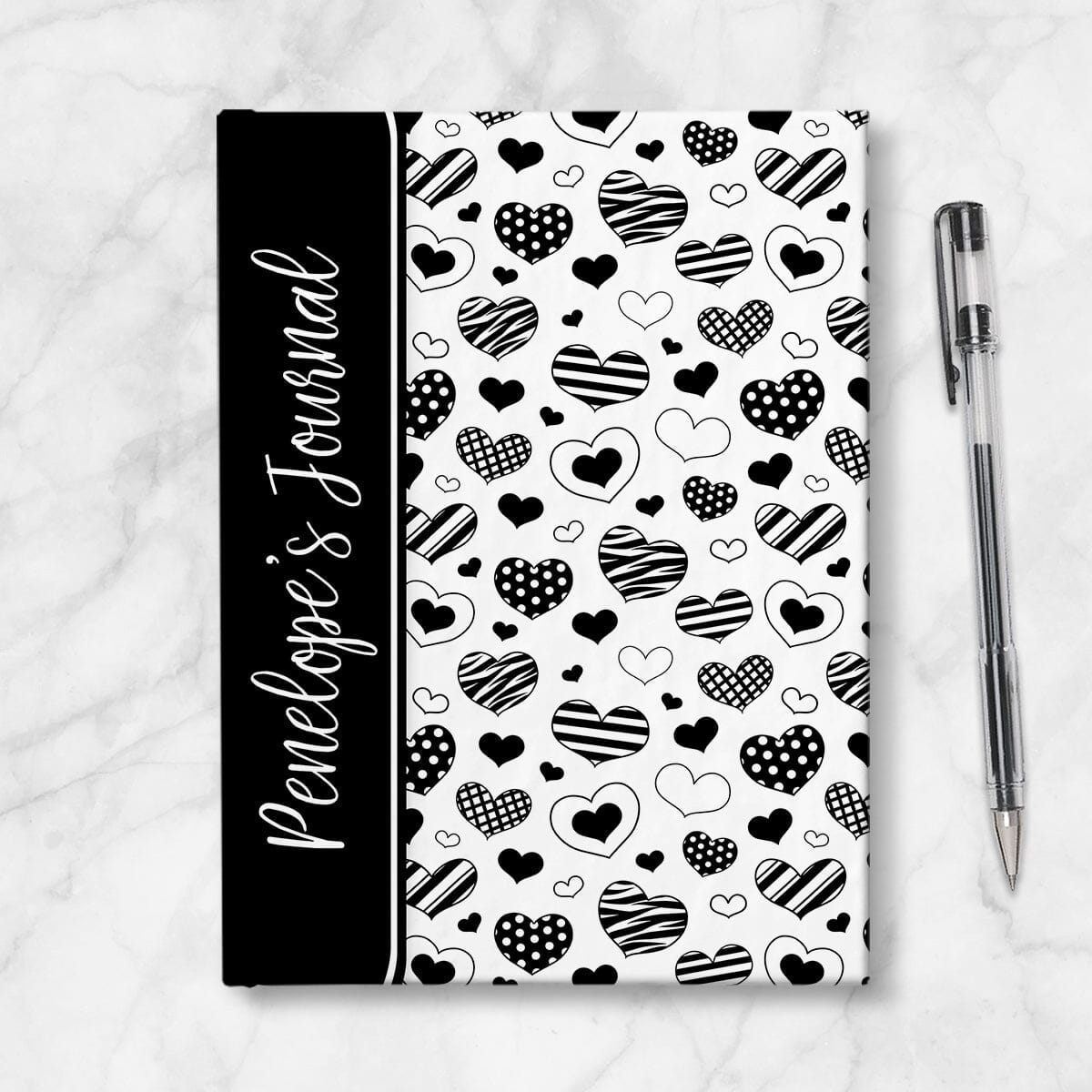 Personalized Black Heart Doodles Journal at Artistically Invited. A custom book featuring a pattern of hand-drawn hearts with different patterns and styles over a white background. Your personalized name is printed in a white handwriting font sideways on the front of the book over a black color block that wraps around the spine area. Image shows the book next to a pen.