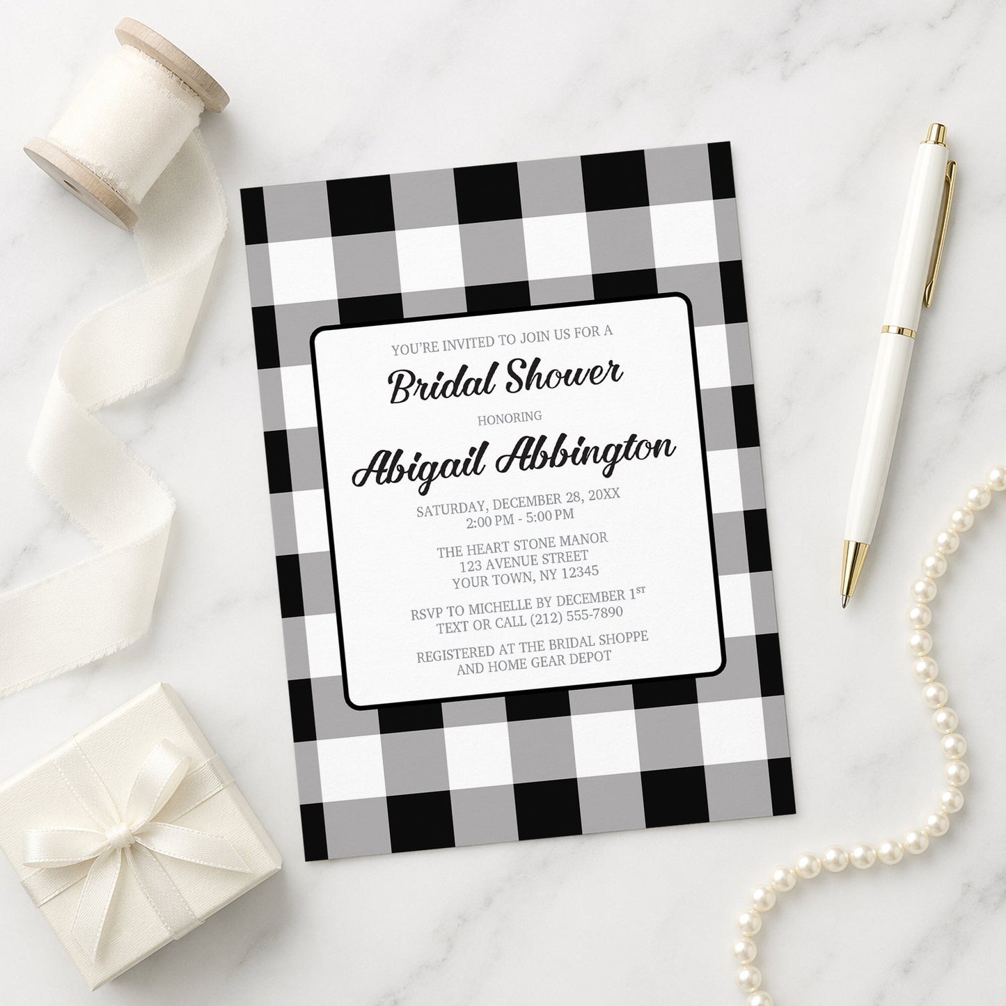 Black and White Buffalo Plaid Bridal Shower Invitation with black and white checkered border on a marble surface with decorative items.