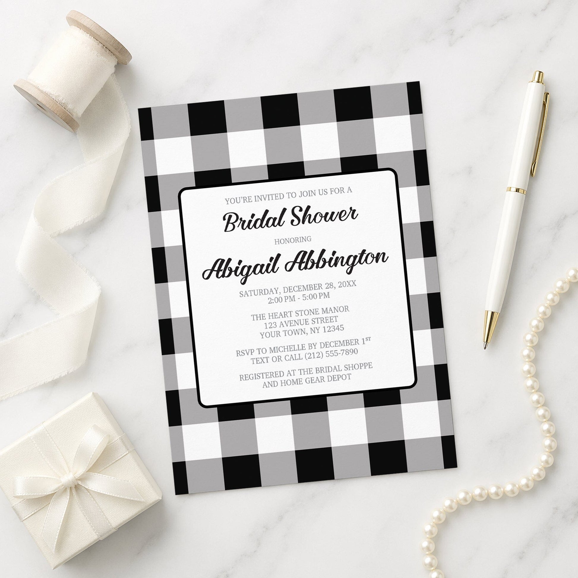 Black and White Buffalo Plaid Bridal Shower Invitation with black and white checkered border on a marble surface with decorative items.