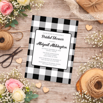 Black and White Buffalo Plaid Bridal Shower Invitation with black and white checkered border on a wooden surface with flowers and twine.