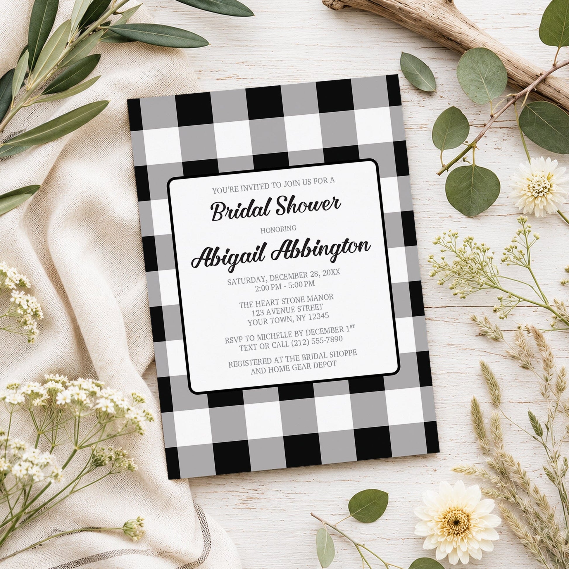 Black and White Buffalo Plaid Bridal Shower Invitation shown on a light wooden surface with spring and summer plants.