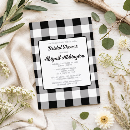 Black and White Buffalo Plaid Bridal Shower Invitation shown on a light wooden surface with spring and summer plants.