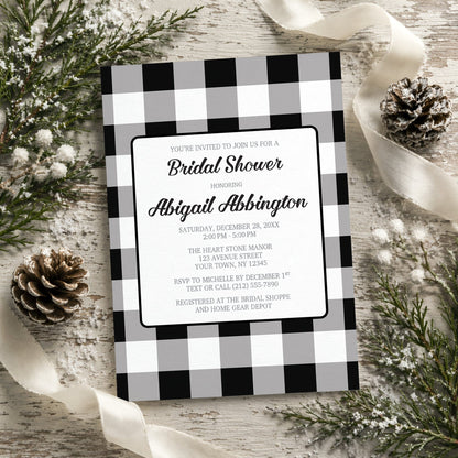 Black and White Buffalo Plaid Bridal Shower Invitation with black and white checkered border on a rustic background with pine cones and ribbons.