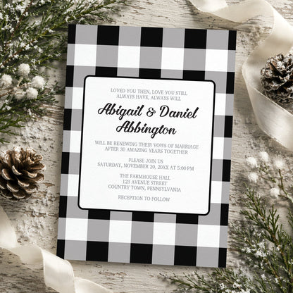 Black and White Buffalo Plaid Vow Renewal Invitation with black and white checkered border shown on a wooden surface with winter greenery and pine cones.