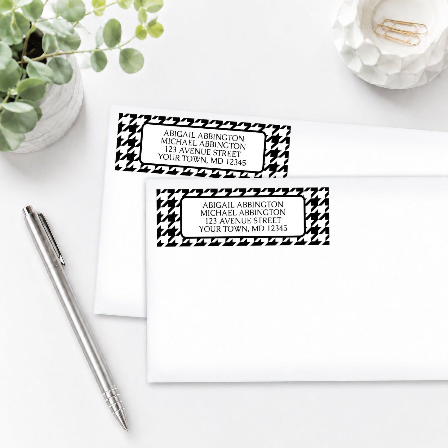 Black and White Houndstooth Address Labels on two white envelopes on a white surface with a plant and a pen.