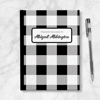 Personalized Black and White Buffalo Plaid Journal at Artistically Invited. Image shows book on table with a pen next to it. 