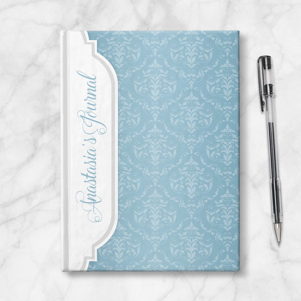 Personalized Blue Damask Journal at Artistically Invited. Image shows the book on a countertop next to a pen.