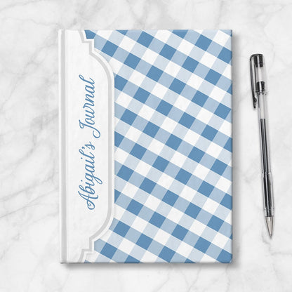 Personalized Blue Gingham Journal at Artistically Invited. Image shows the book on a countertop next to a pen.