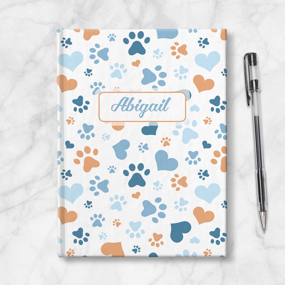Personalized Blue Hearts and Paw Prints Journal at Artistically Invited. Image shows the book on a countertop next to a pen.