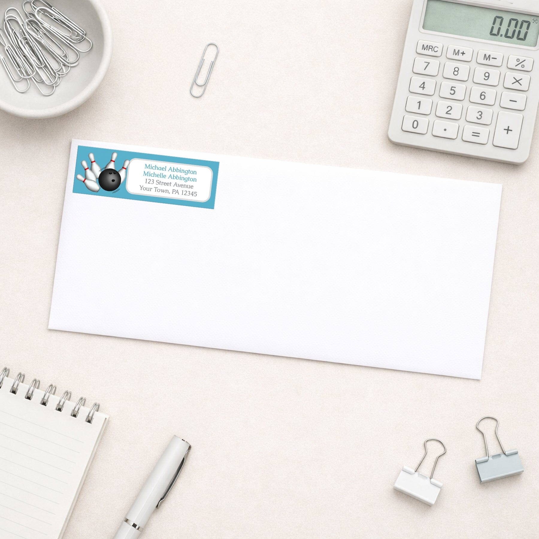 Blue Bowling Return Address Label shown on a white envelope with everyday office supplies