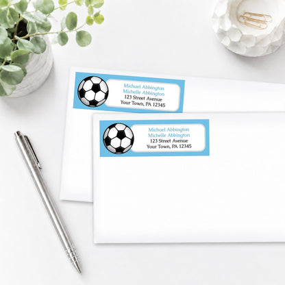 Blue Soccer Ball Address Labels on white envelopes, shown on a white surface with a plant and a pen.
