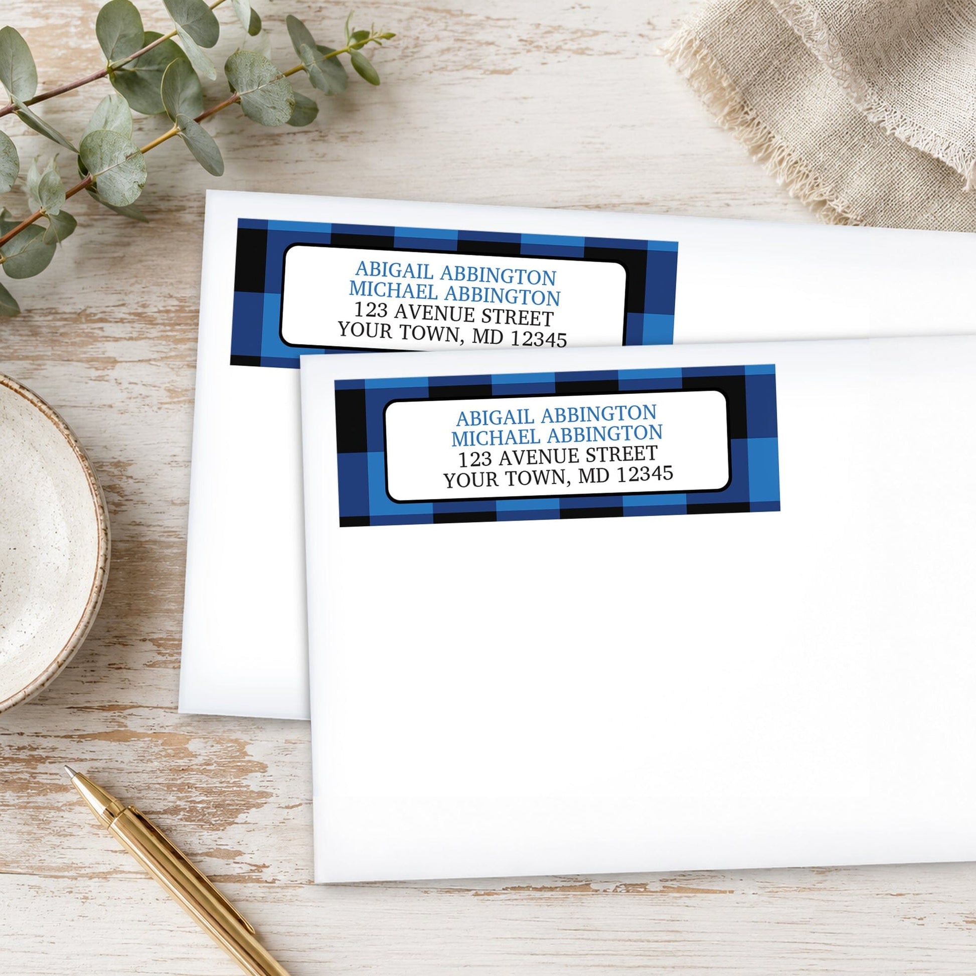 Blue and Black Buffalo Plaid Address Labels on white envelopes, shown on a wooden surface with plants and a pen.