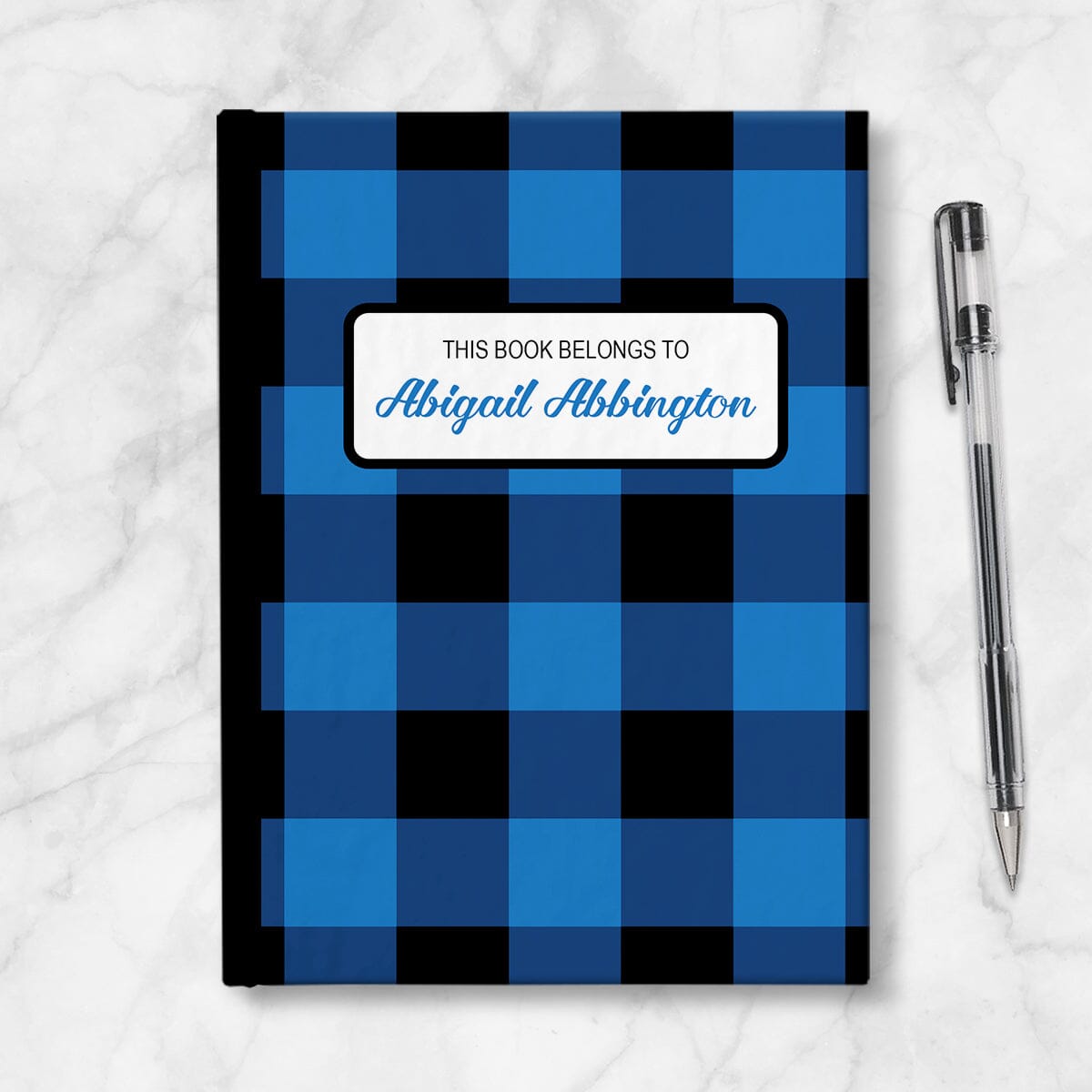 Personalized Blue and Black Buffalo Plaid Journal at Artistically Invited. Image shows the book on a countertop next to a pen.