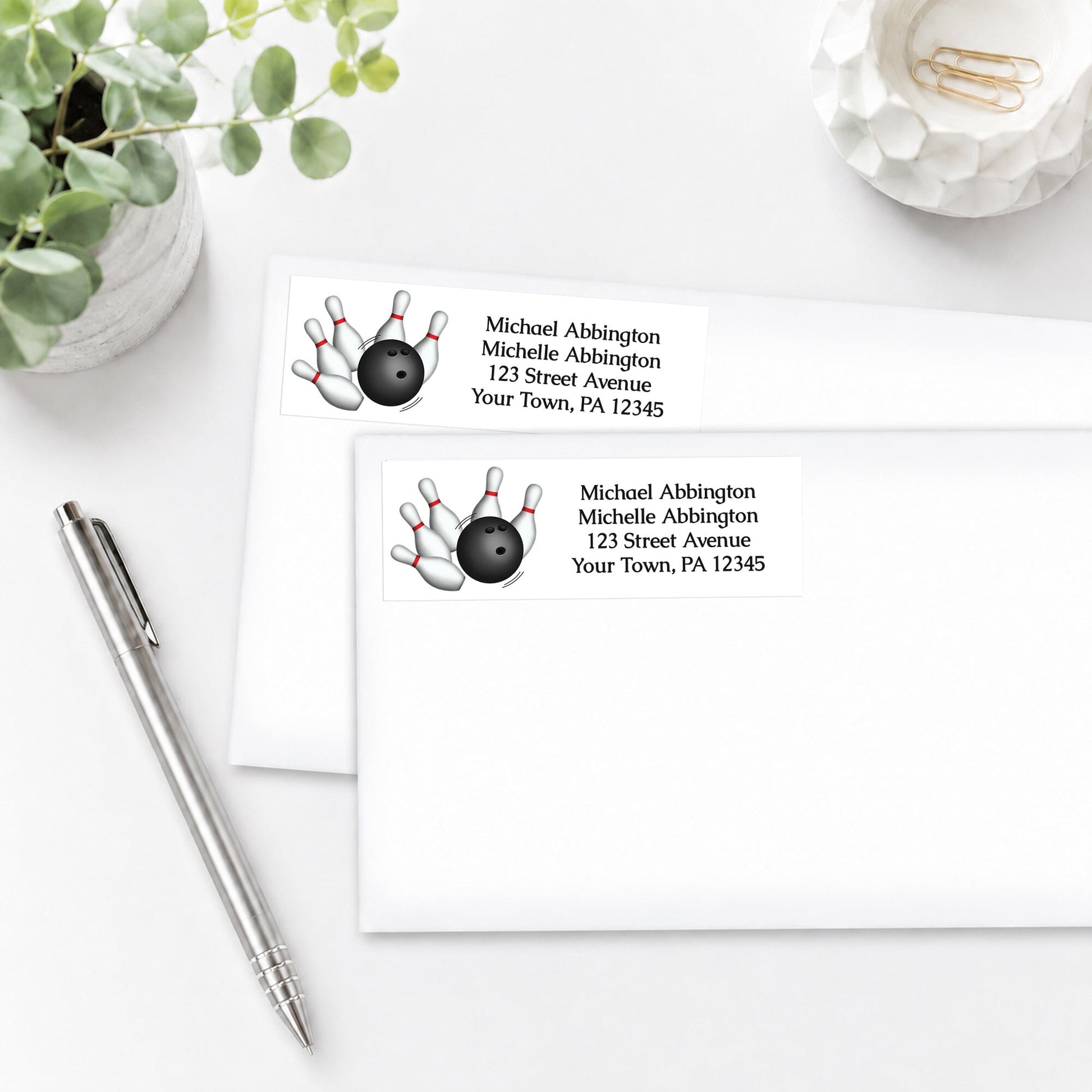 Address labels with bowling design, shown on white envelopes, on a white surface with a pen and plant.