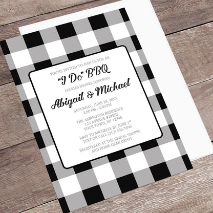 Black and White Buffalo Plaid I Do BBQ Couples Shower Invitation shown at an angle on a brown wood surface with a white envelope.