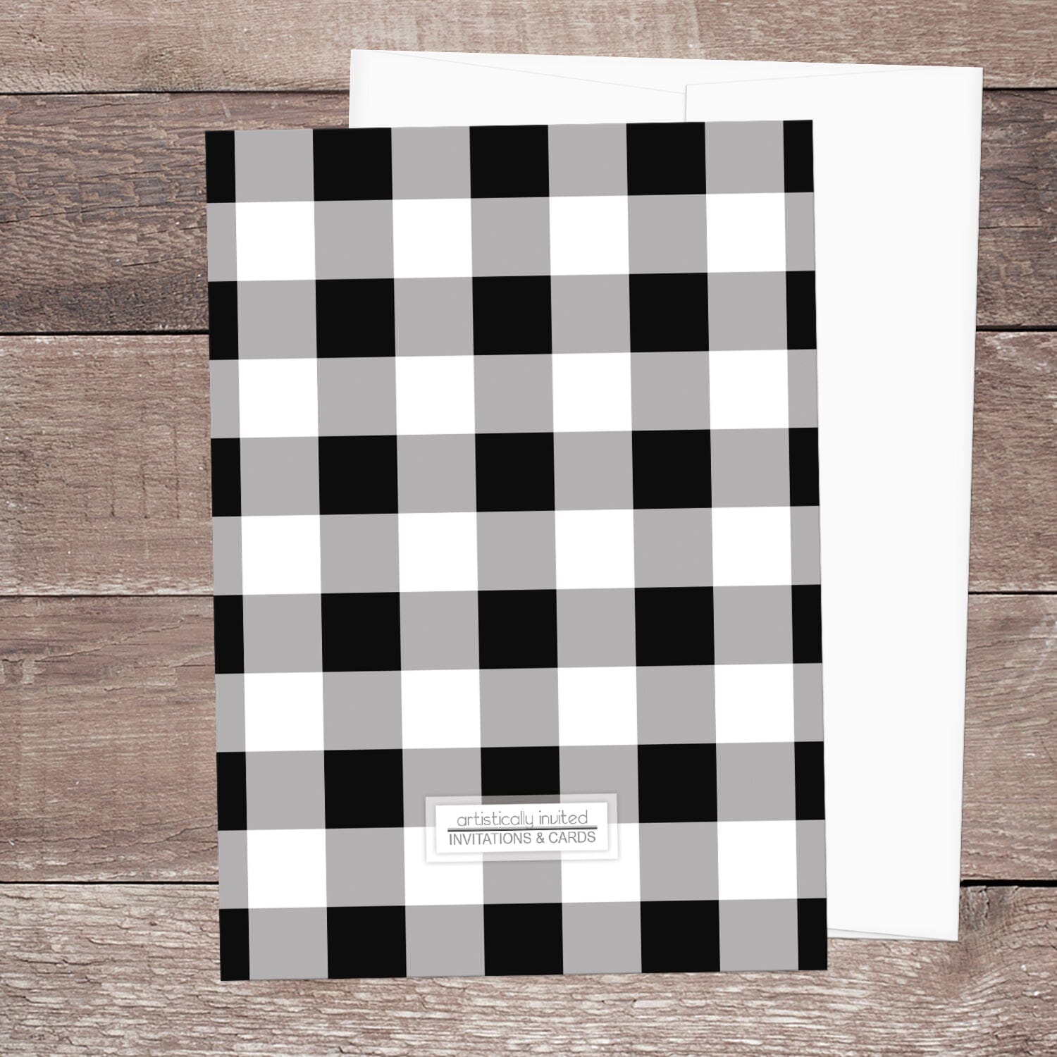 The back side of the Black and White Buffalo Plaid I Do BBQ Couples Shower Invitation, featuring the black and white check pattern, shown on a brown wood surface with a white envelope.