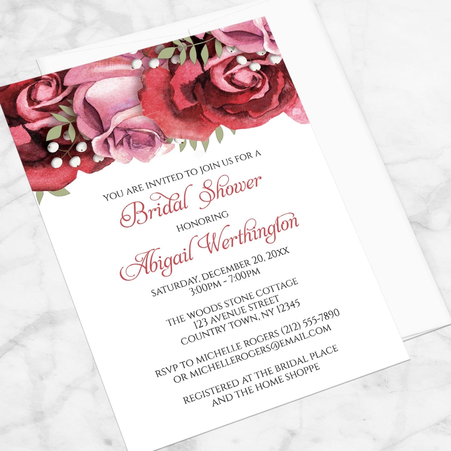 Bridal shower invitation with burgundy-red and pink roses along the top, displayed at an angle with a white envelope on a marble surface
