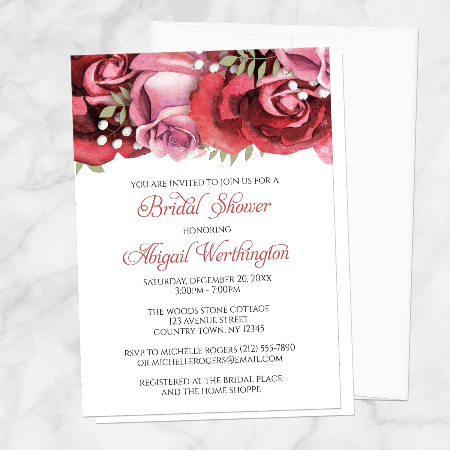Bridal shower invitation with burgundy-red and pink roses along the top, displayed with a white envelope on a marble surface