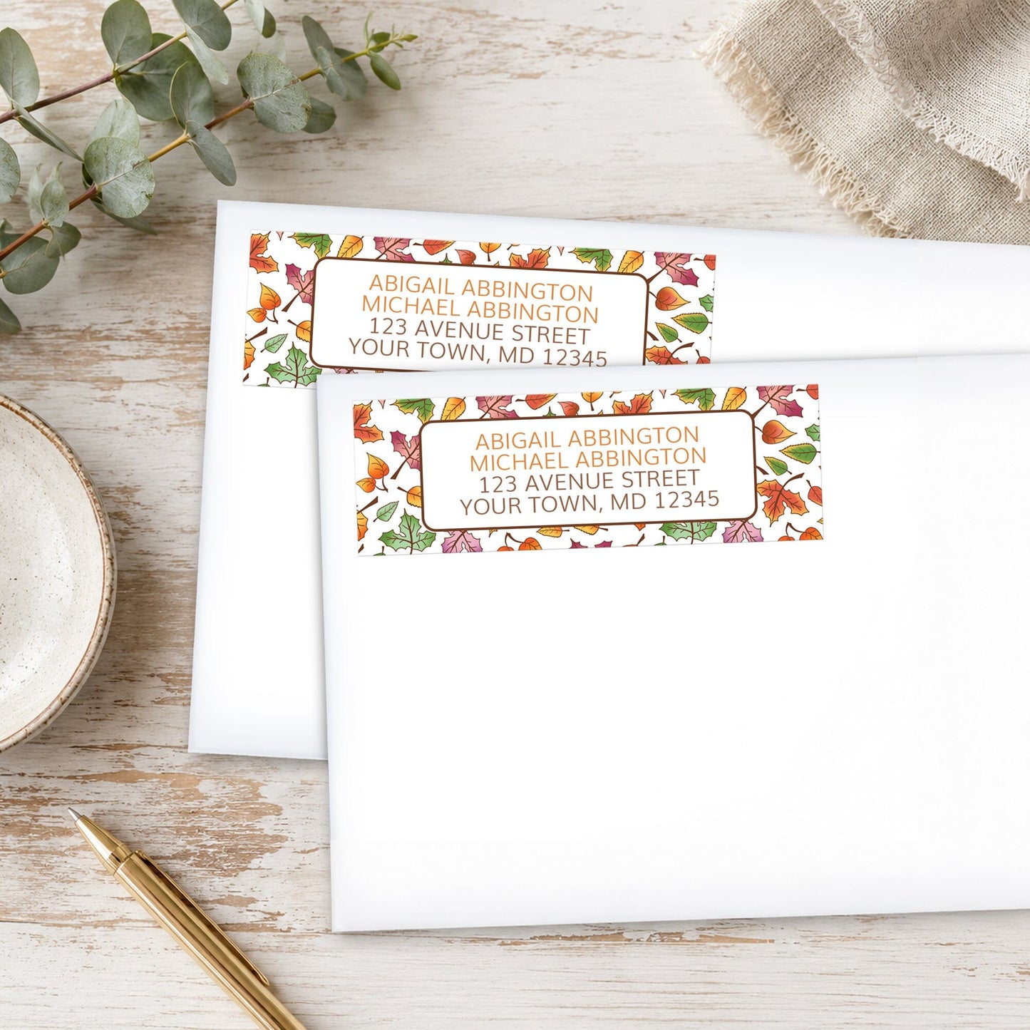 Changing Leaves Fall Address Labels with fall leaf design on white envelopes, placed on a wooden surface with eucalyptus leaves and a pen.