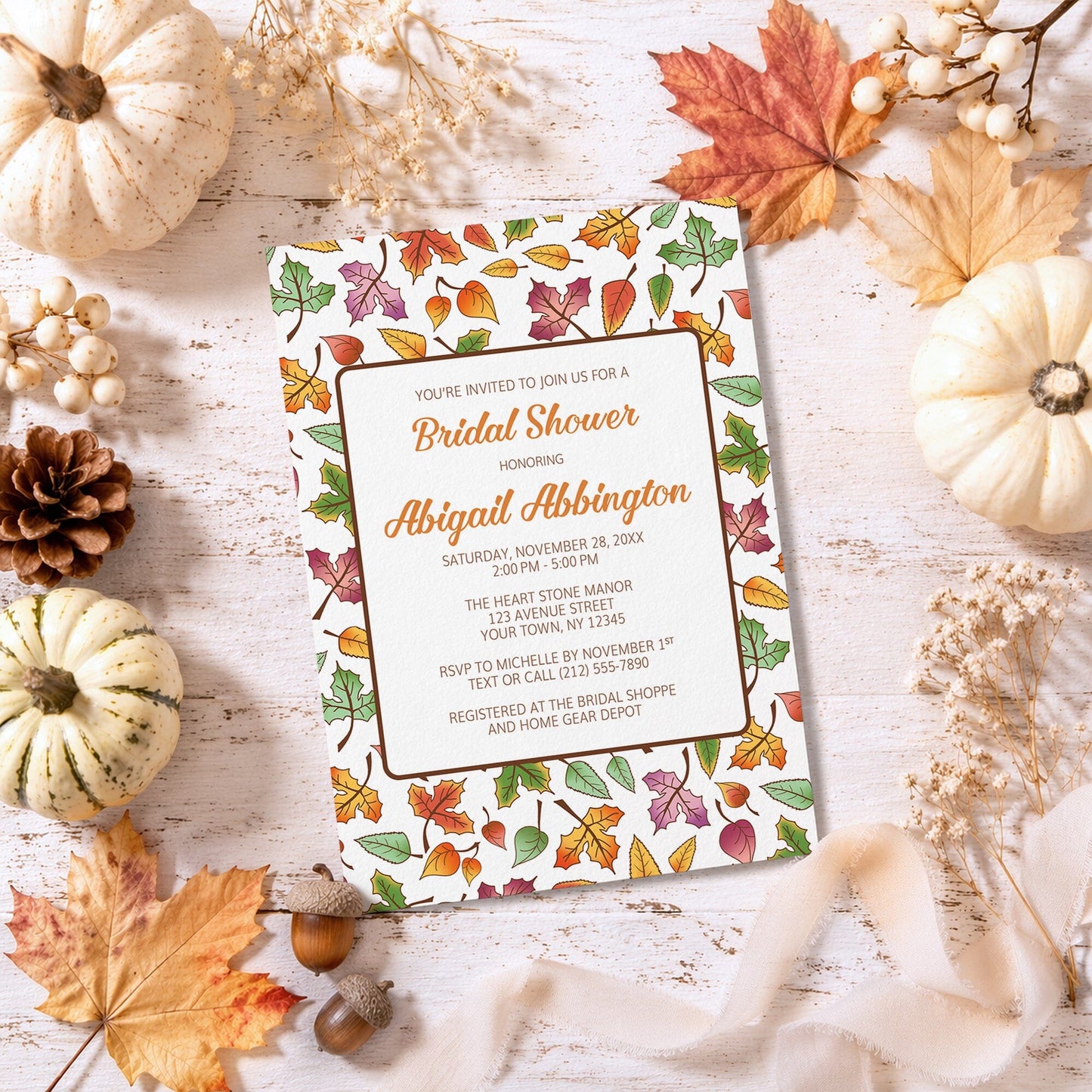 Bridal shower invitation with autumn leaf design surrounded by fall pumpkins and leaves on a wooden surface