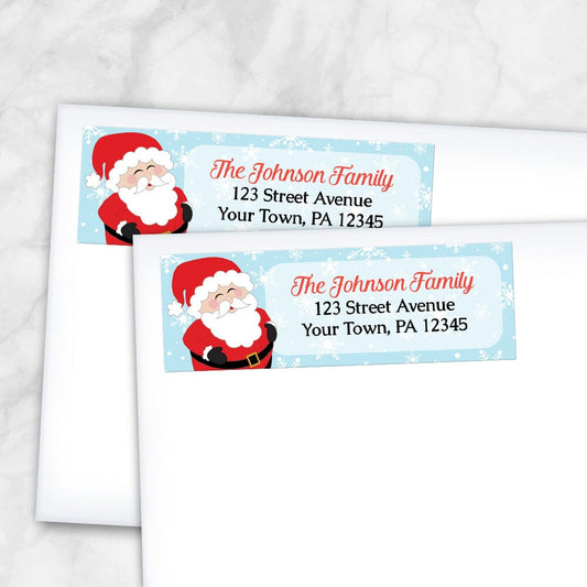 Cheerful Santa Address Labels at Artistically Invited. Cute return address labels illustrated with a cheerful and jolly Santa Claus, holding his belly and laughing, on the left side of the labels over a light blue winter background with white snowflakes. Your personalized return address is custom printed in red and black to the right of the cute Santa Claus over a lighter rectangular area of the light blue background. Example shows the labels on envelopes.