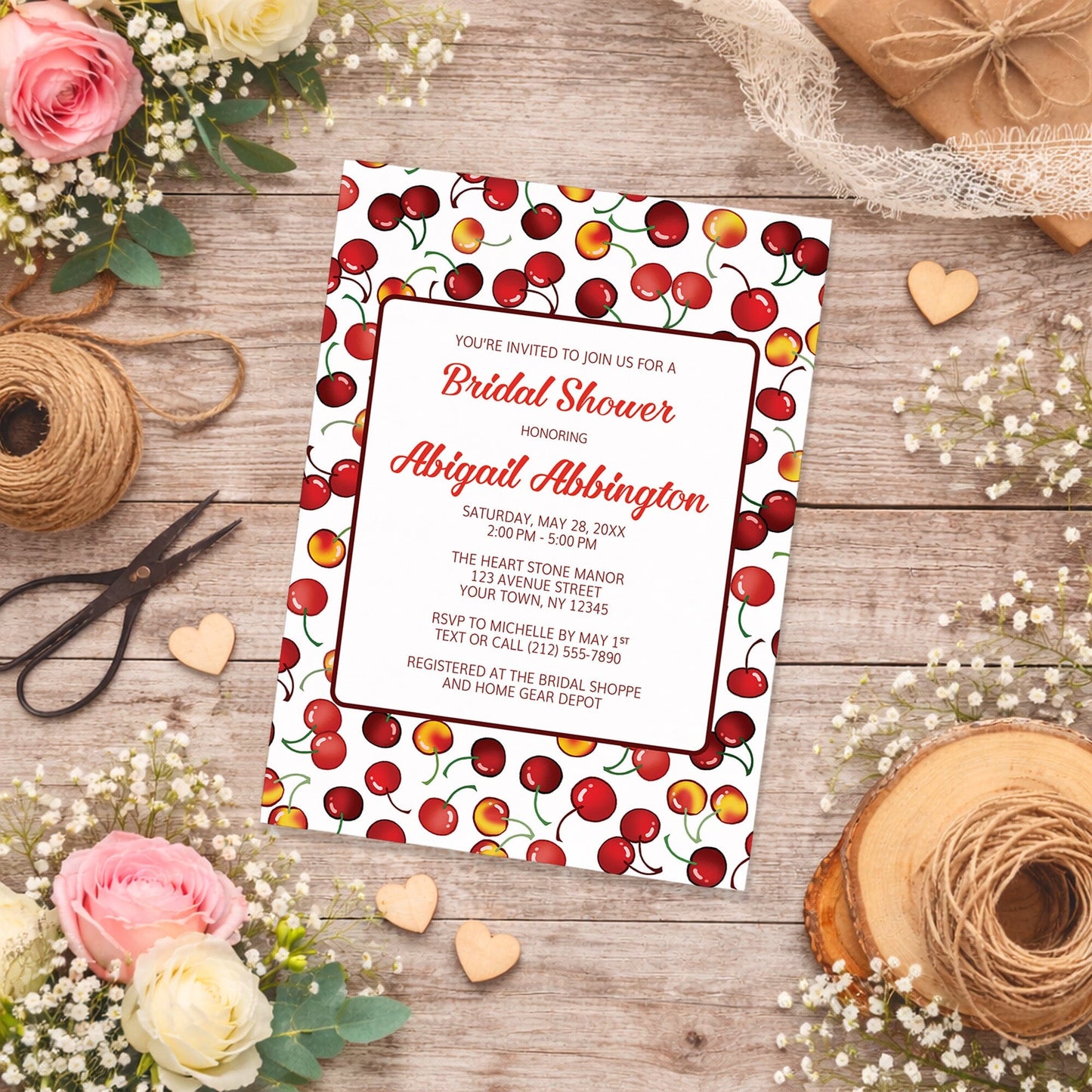 Cherries Bridal Shower Invitation on a wooden surface with flowers and twine.