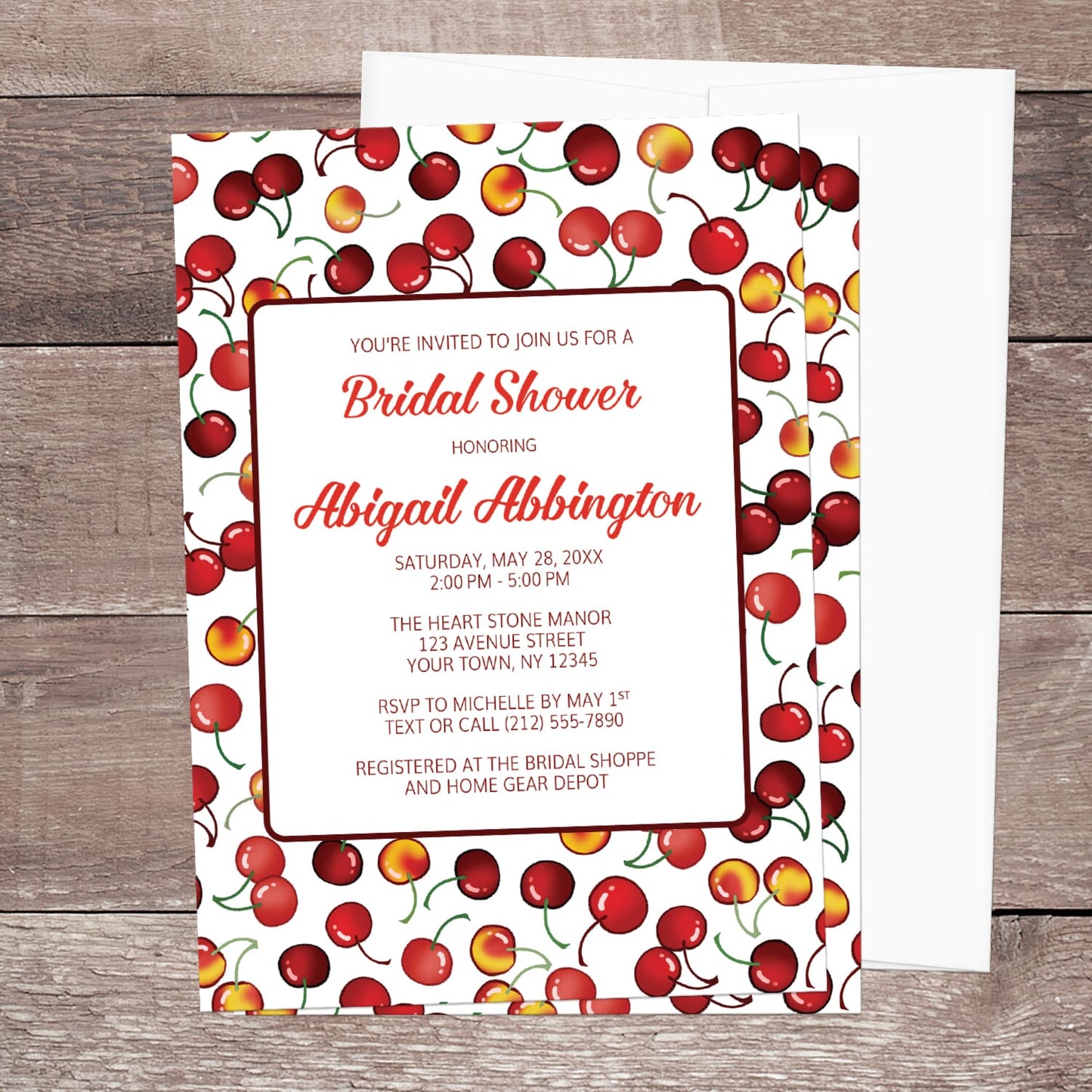 Bridal shower invitation with cherry design, displayed with a white envelope on a wooden surface