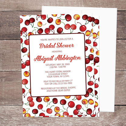 Bridal shower invitation with cherry design, displayed with a white envelope on a wooden surface