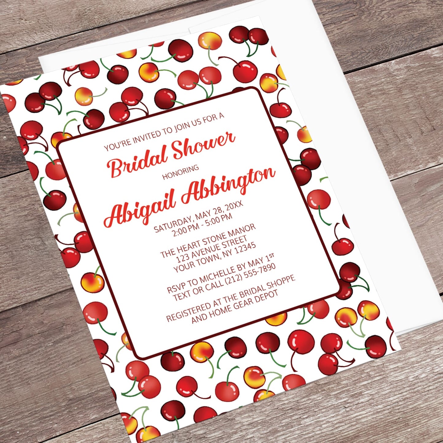 Bridal shower invitation with cherry design, displayed in an angle view with a white envelope on a wooden surface