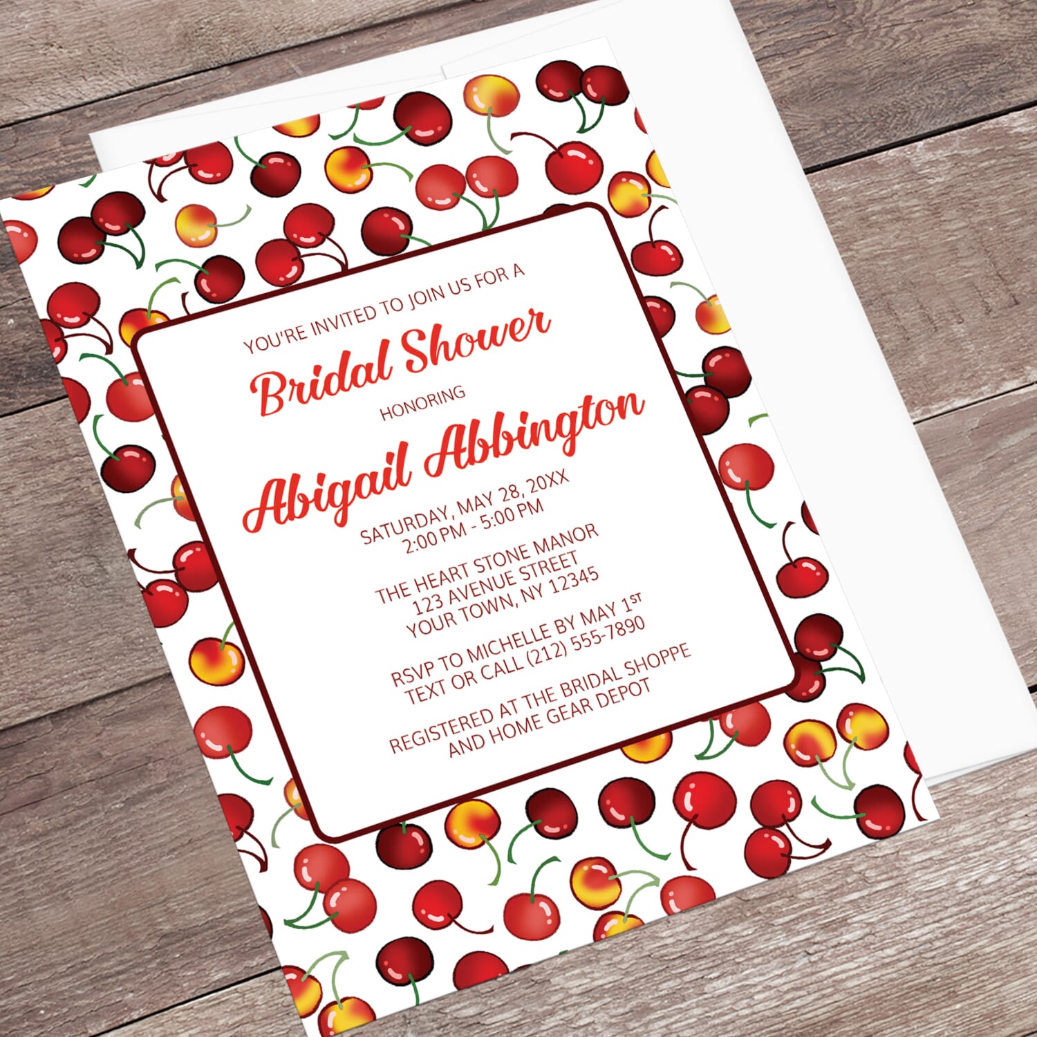 Bridal shower invitation with cherry design, displayed in an angle view with a white envelope on a wooden surface