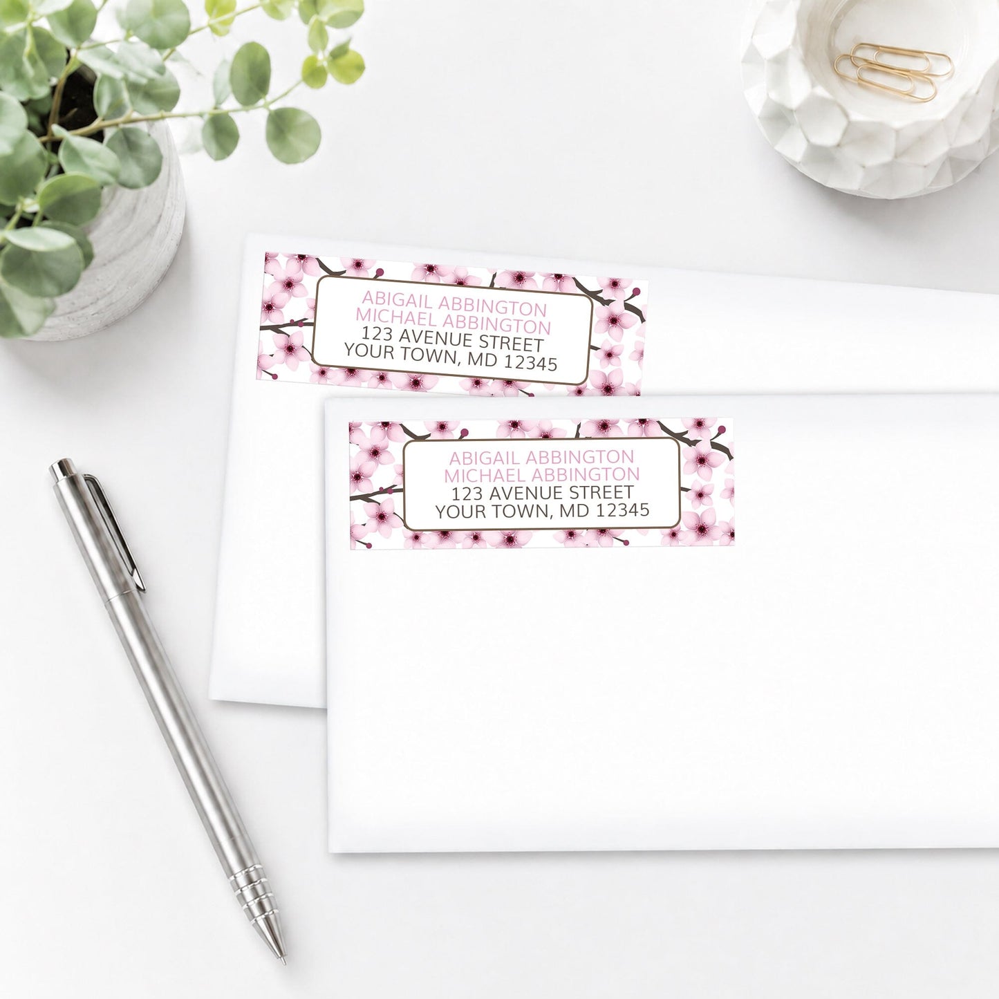 Cherry Blossom Address Labels, shown on white envelopes, on a white surface with a plant and a pen.