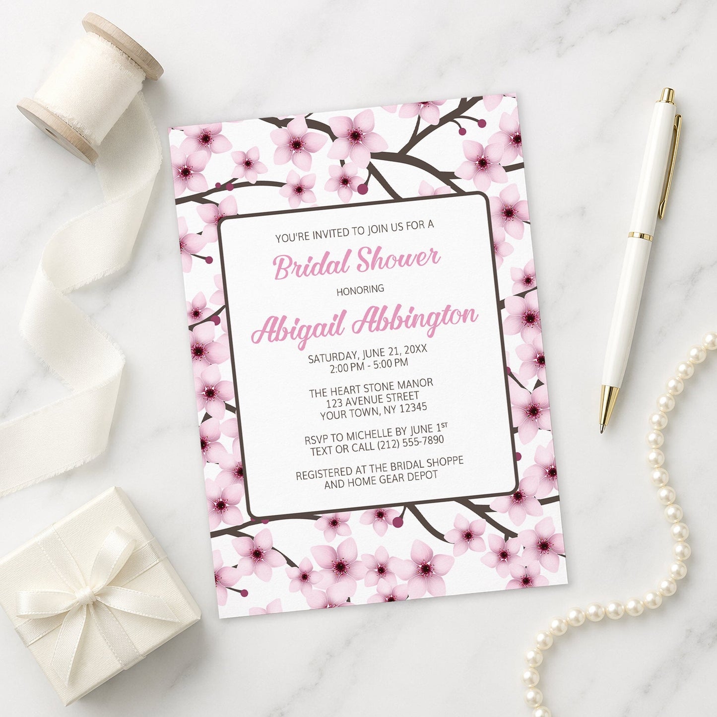 Cherry Blossom Bridal Shower Invitation on a marble surface with ribbon and pen.