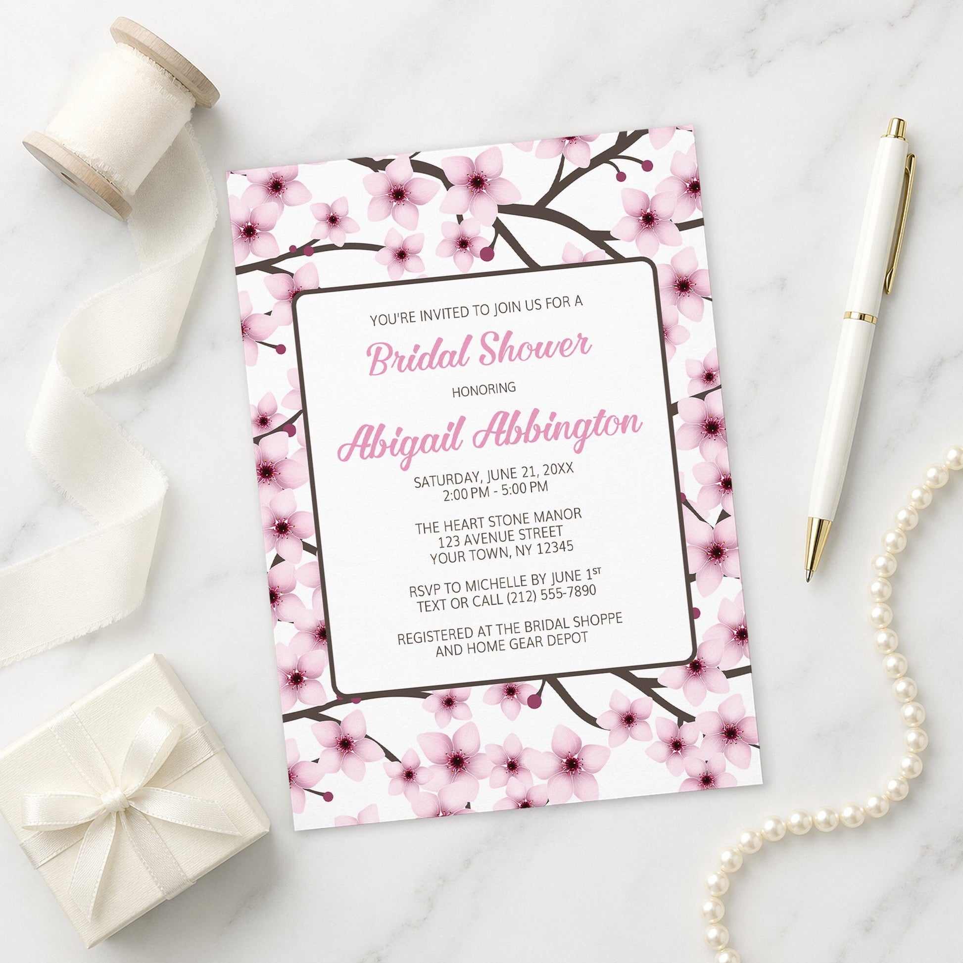 Cherry Blossom Bridal Shower Invitation on a marble surface with ribbon and pen.