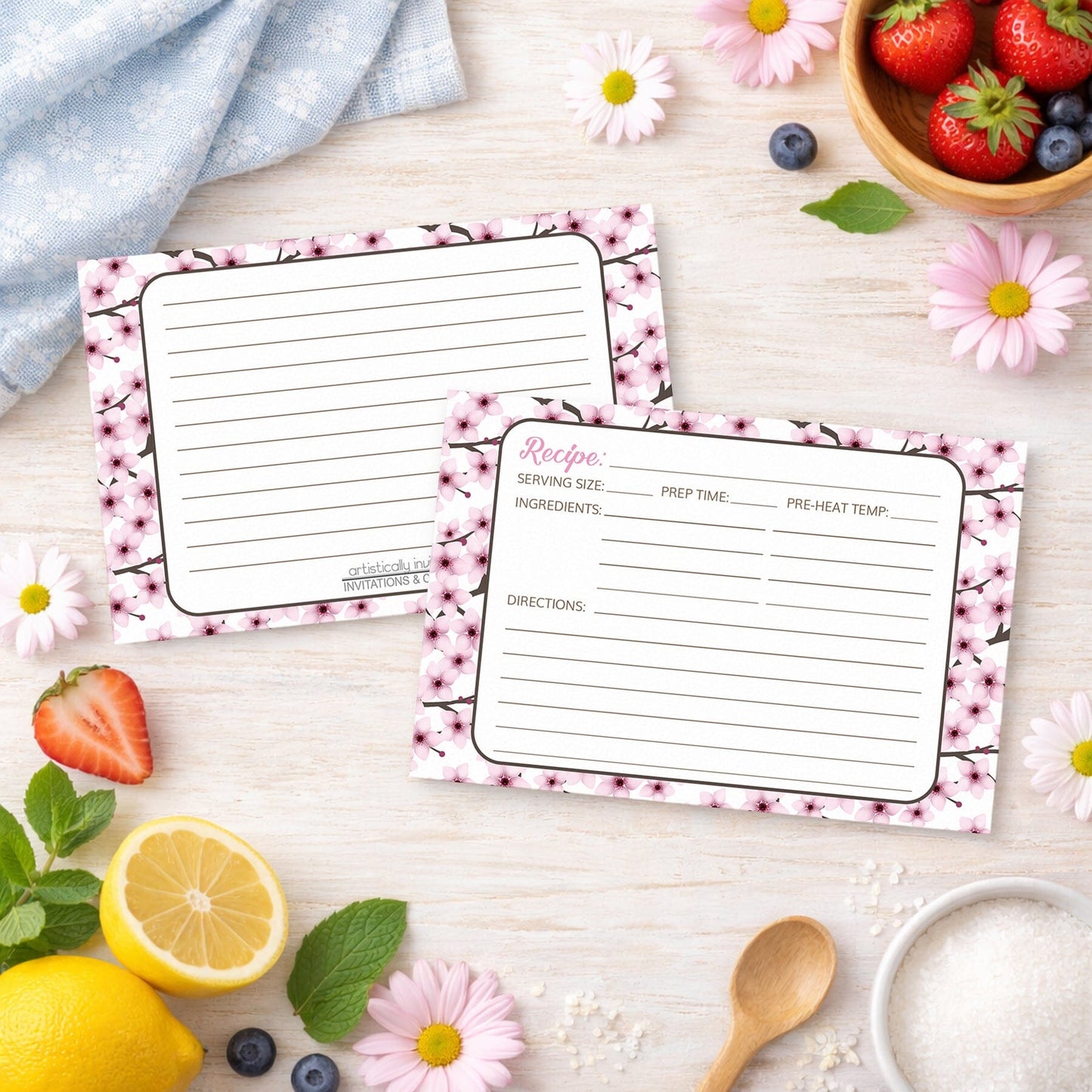 Two Cherry Blossom Recipe Cards on a wooden surface with spring and summer fruits and flowers.
