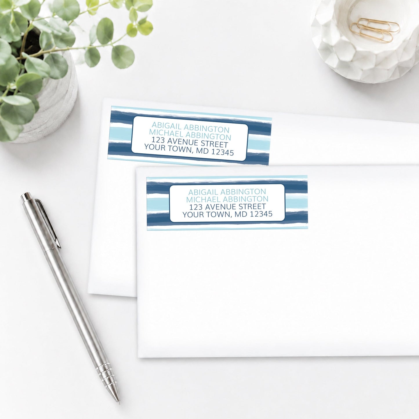 Coastal Paint Brush Strokes Address Labels shown on white envelopes on a white surface with a plant and a pen.