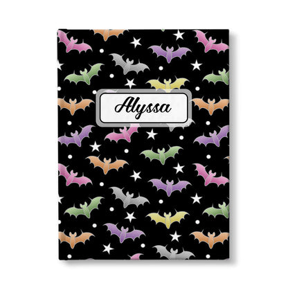 Colorful Bats Journal at Artistically Invited. A journal designed with a pattern of bats in different colors over a black background color that wraps around the book. Your personalized name is custom printed in a black script font in a white rectangular design over the bats pattern. Available with ruled lines or blank inside.