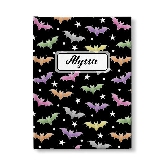 Colorful Bats Journal at Artistically Invited. A journal designed with a pattern of bats in different colors over a black background color that wraps around the book. Your personalized name is custom printed in a black script font in a white rectangular design over the bats pattern. Available with ruled lines or blank inside.