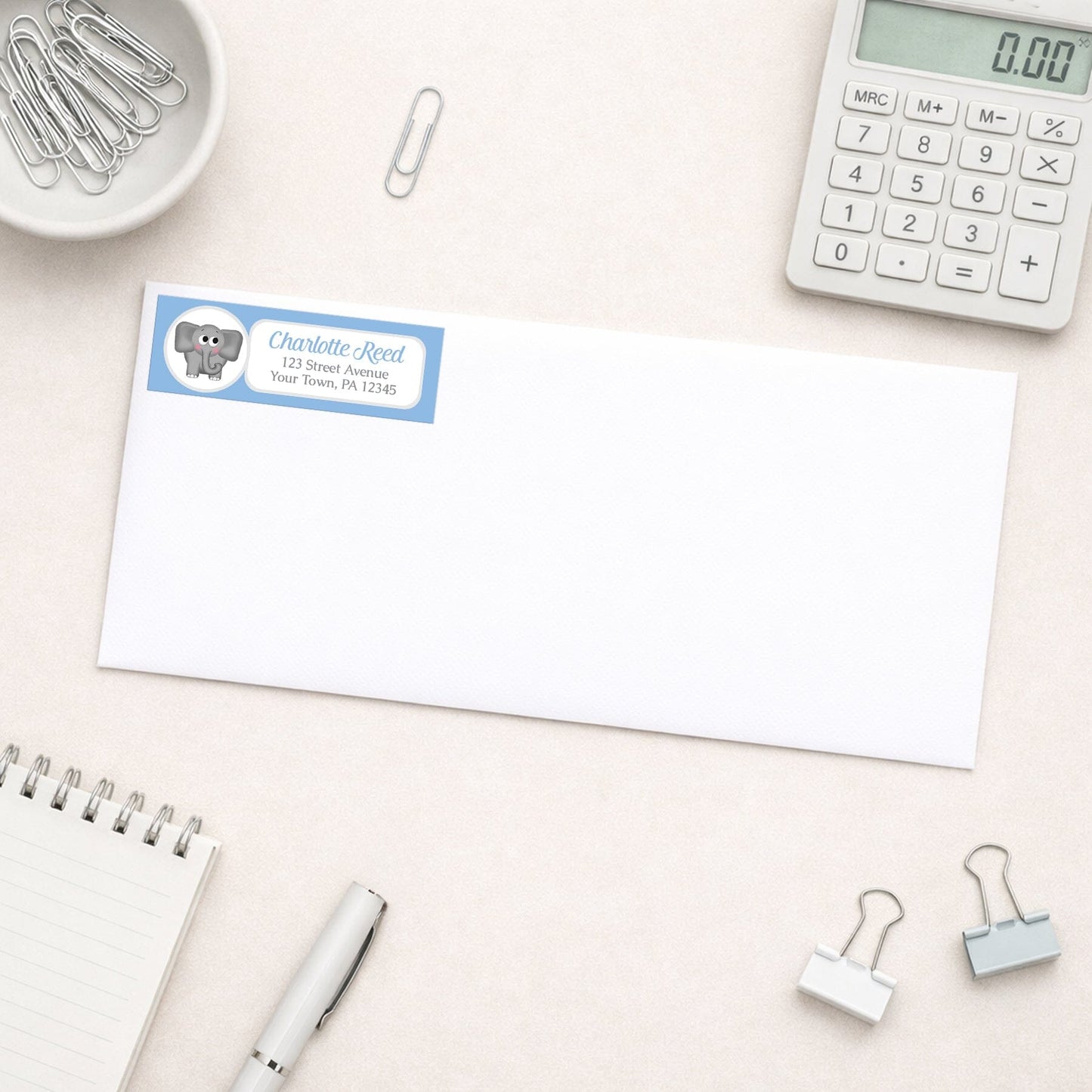 Cute Elephant Blue Address Label shown on a white envelope with everyday office supplies