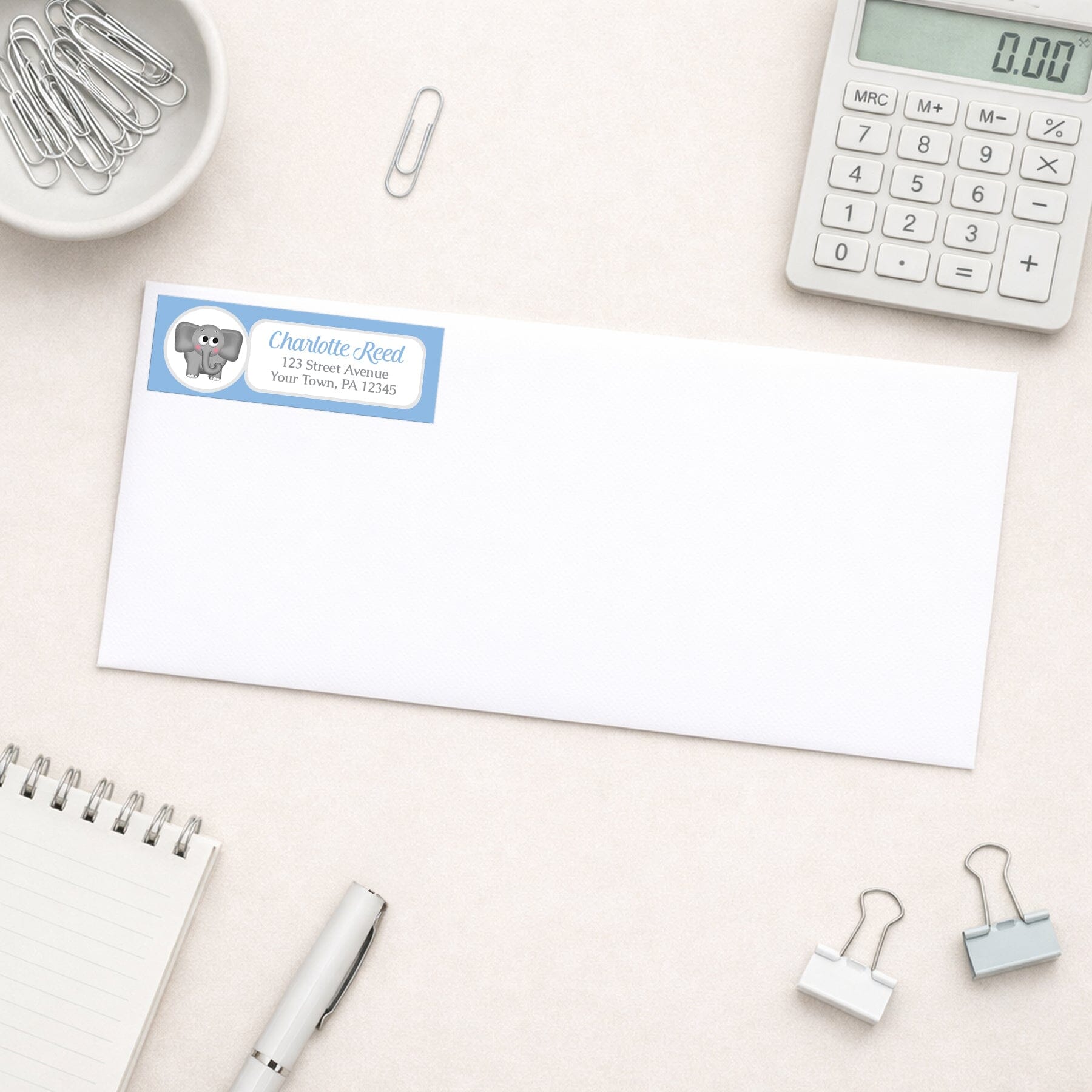 Cute Elephant Blue Address Label shown on a white envelope with everyday office supplies
