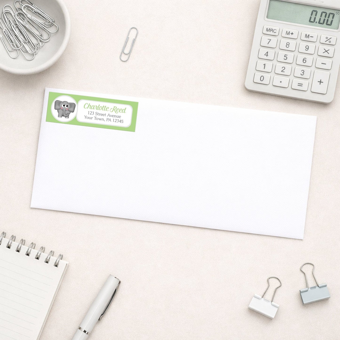 Cute Elephant Green Address Label shown on a white envelope with everyday office supplies